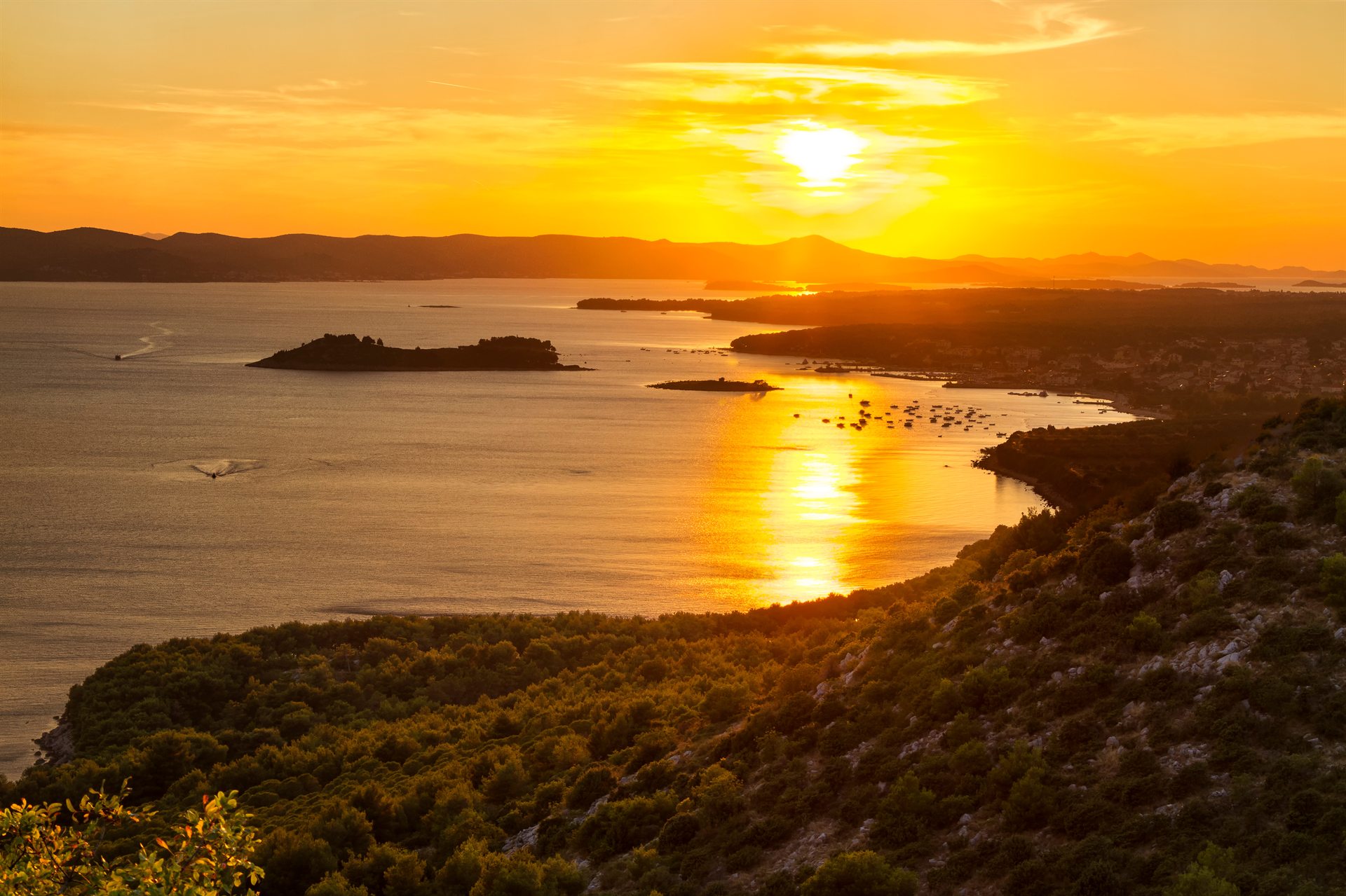 Zachód słońca nad zatoką z złotym odbiciem na wodzie, wyspami i zalesionym zboczem