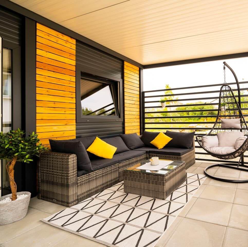 Taras z rattanową narożną sofą i żółtymi poduszkami, wisząca huśtawka koszowa i geometryczny dywan