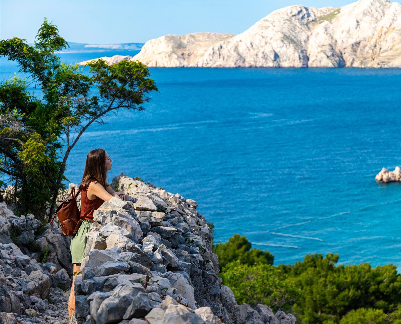 Kobieta z plecakiem stojąca na skalnym urwisku, patrząca na lazurowe morze i jasne wapienne klify