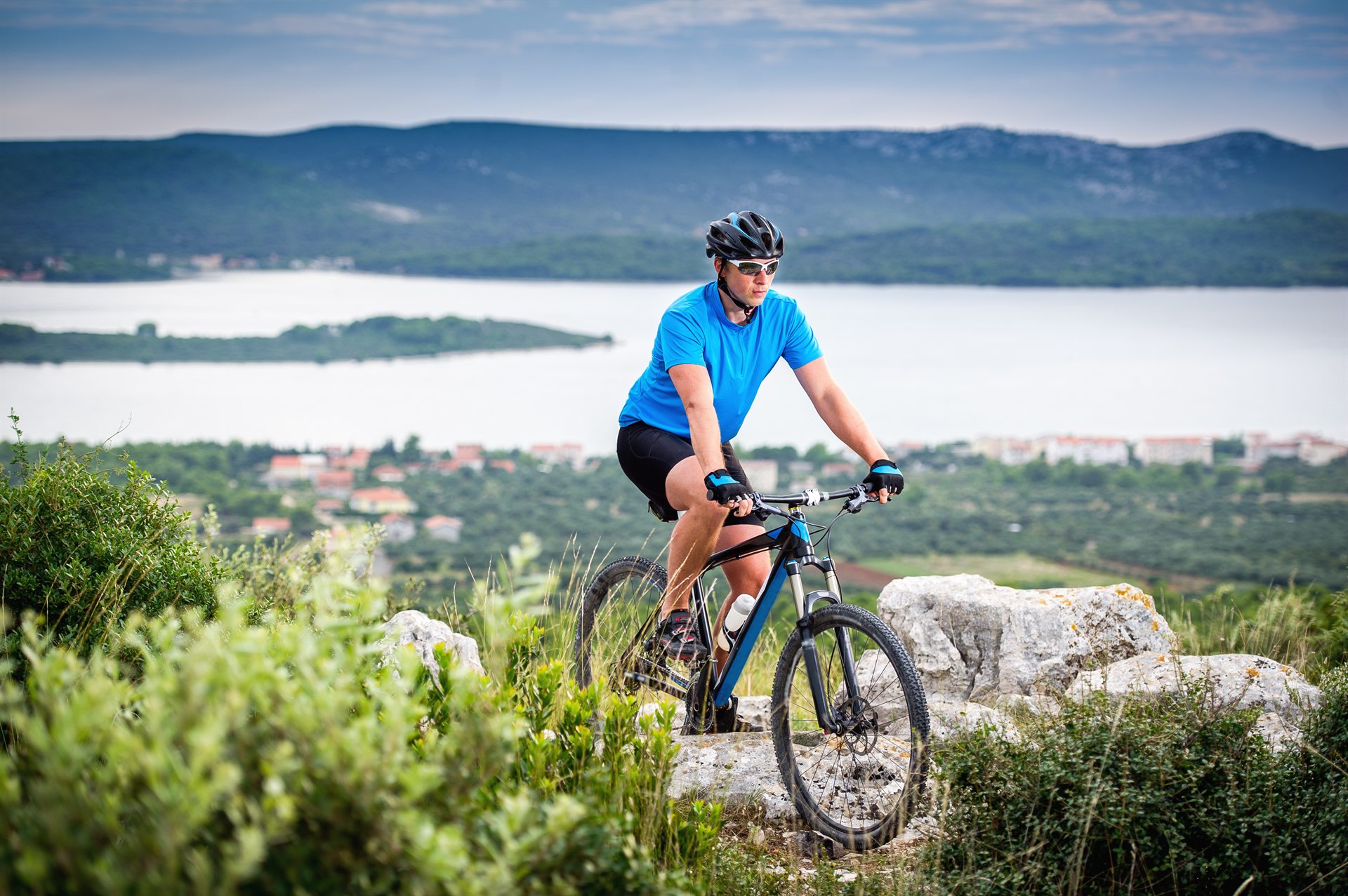 Kolarz w niebieskiej koszulce na górskim rowerze na skalnym szlaku z widokiem na morze i wyspy